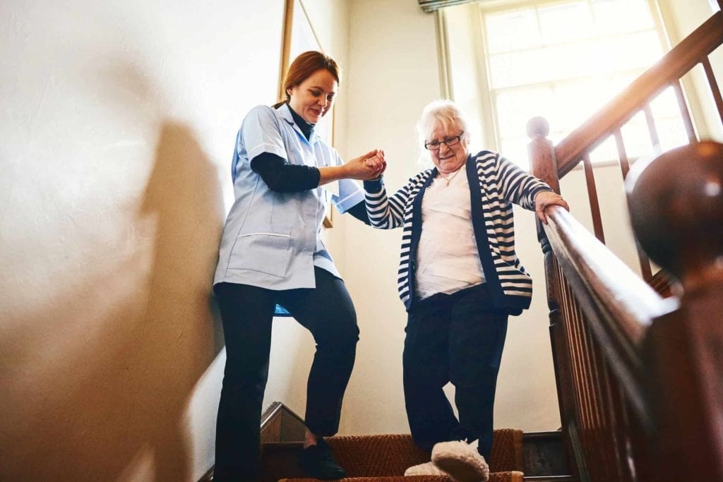 Habilidades de um cuidador de idosos - cuidadora ajudando uma idosa a descer as escadas